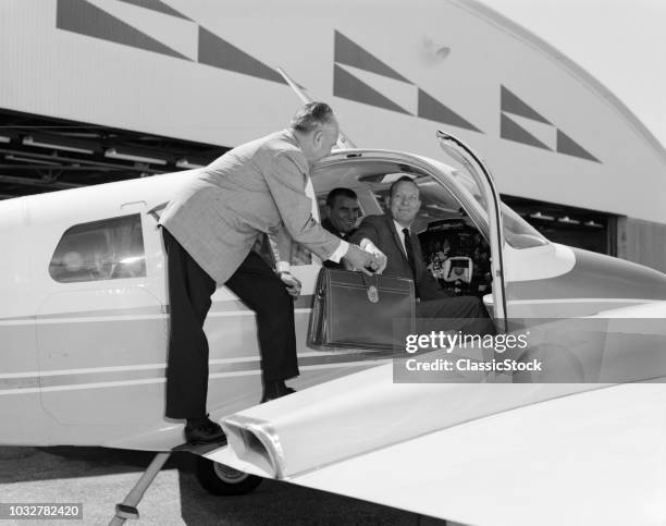 1960s SMILING BUSINESSMEN IN CESSNA 310G TWIN ENGINE AIRPLANE MAN HANDING LEATHER BRIEFCASE TO PASSENGER