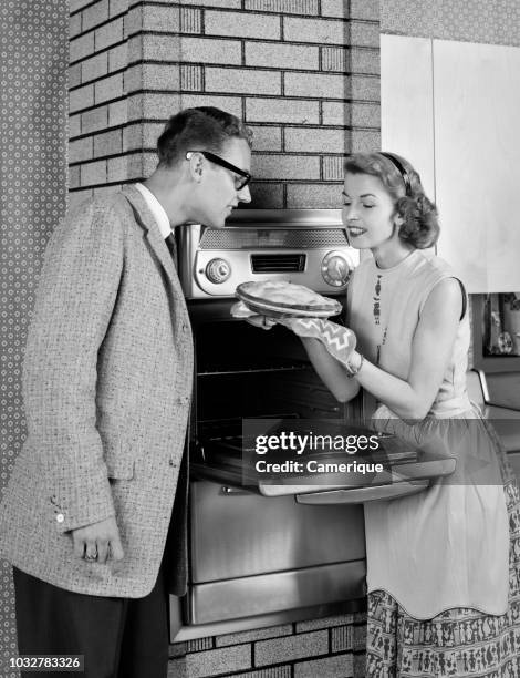 1950s COUPLE IN KITCHEN WOMAN SHOWING FRESHLY BAKED PIE TO MAN