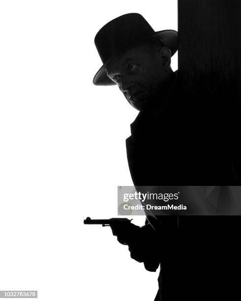 1950s ANONYMOUS SILHOUETTE OF MAN WEARING FEDORA HAT PEEKING AROUND CORNER WITH PISTOL IN HAND