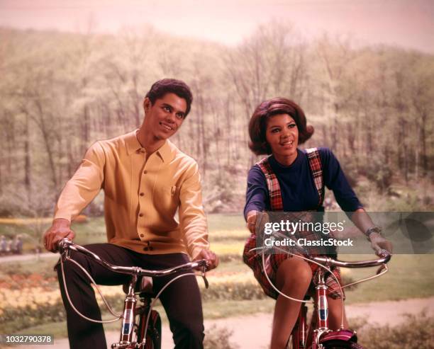 1960s AFRICAN AMERICAN TEENAGE BOY AND GIRL RIDING BICYCLES