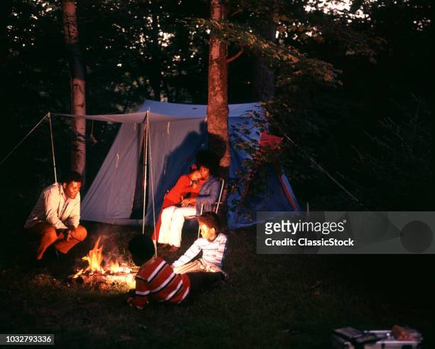 1970s AFRICAN AMERICAN FAMILY CAMPING WITH TENT NIGHT SHOT SITTING AROUND CAMPFIRE