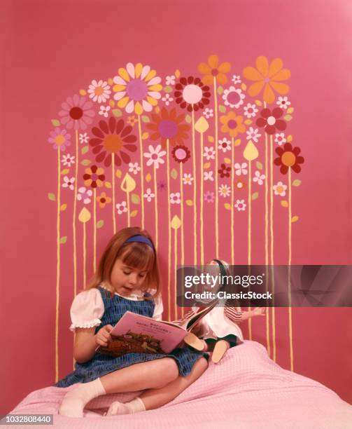 1970s GIRL SITTING BED READING TO DOLL PINK WALLS BEDROOM HEADBOARD MADE OF COLORFUL FLOWER SHAPES GLUED TO WALL