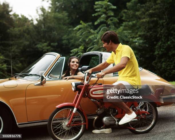 1970s MAN ON SMALL RED HARLEY DAVIDSON WOMAN IN GOLD PORSCHE TALKING FLIRT COUPLE MOTORCYCLE LIFESTYLE