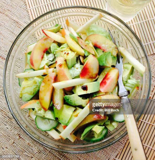 chopped pink lady apple, white nectarine, avocado and cucumber salad in a clear salad bowl, with lemon infused olive oil, fig infused balsamic vinegar dressing and a antique fork and glass of white grape juice - nektarine stock-fotos und bilder