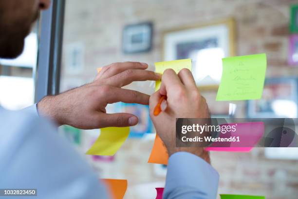 close-up of man in office writing on adhesive note on glass wall - the workshop stock pictures, royalty-free photos & images