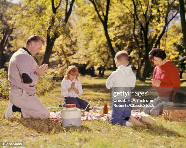 1960s FAMILY KNEELING AROUND PICNIC IN GRASS AUTUMN DAY SAYING GRACE PRAYER