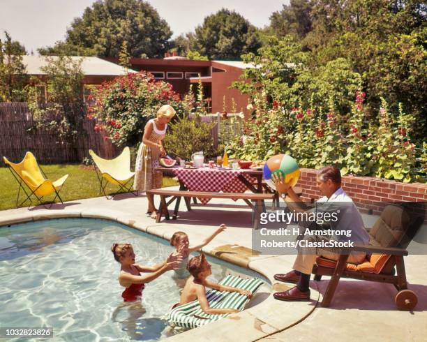 1950s 1960s FAMILY AROUND BACKYARD SWIMMING POOL MOTHER AT PICNIC TABLE FATHER PLAYING BALL WITH KIDS IN POOL