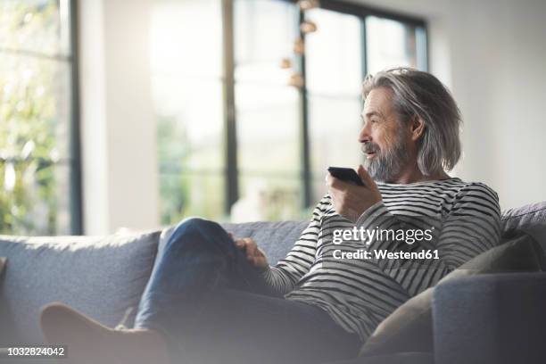 senior man sitting on couch, using smartphone - mann handy couch stock-fotos und bilder