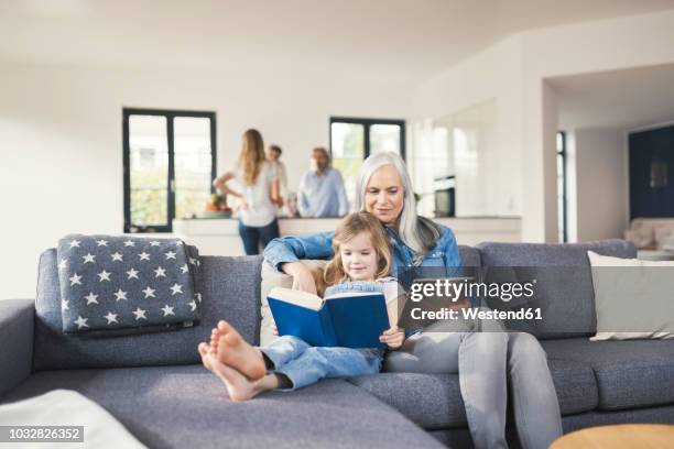 grandmother and granddaughter sitting on couch, reading together book and tablet pc - grandmas living room 個照片及圖片檔