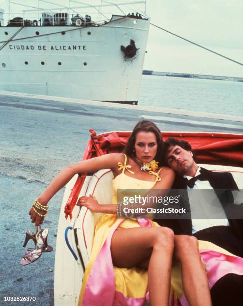 1970s EXHAUSTED CRUISE SHIP PARTY COUPLE IN OPEN CAB MAN IN TUXEDO ASLEEP AGAINST ANGRY WOMAN HOLDING SHOES LOOKING AT CAMERA