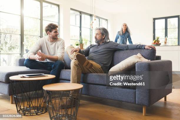 son sitting on couch, talking to his father - millennial generation stock-fotos und bilder