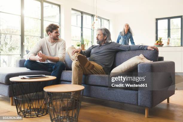 son sitting on couch, talking to his father - adult child stock pictures, royalty-free photos & images