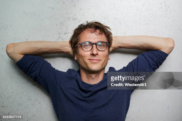 portrait of smiling man with hands behind head wearing glasses - soddisfazione foto e immagini stock
