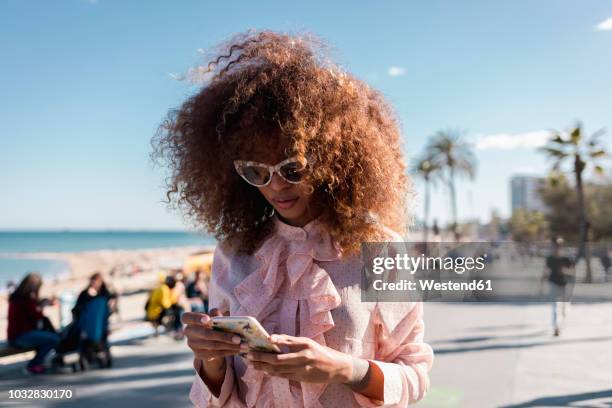 stylish young woman using cell phone at seaside promenade - red blouse fotografías e imágenes de stock