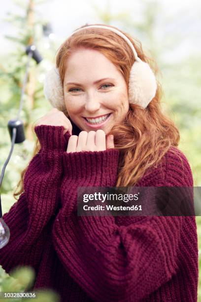 portrait of happy redheaded young woman wearing ear muff and knit pullover - earmuffs foto e immagini stock