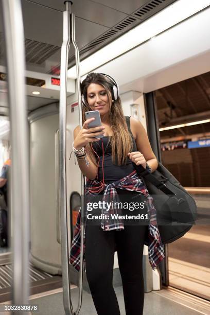 portrait of smiling woman with guitar backpack and headphones looking at cell phone in underground train - passenger muzikant stockfoto's en -beelden