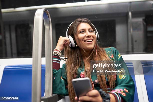 portrait of happy woman listening music with headphones and smartphone in underground train - passagierzug stock-fotos und bilder