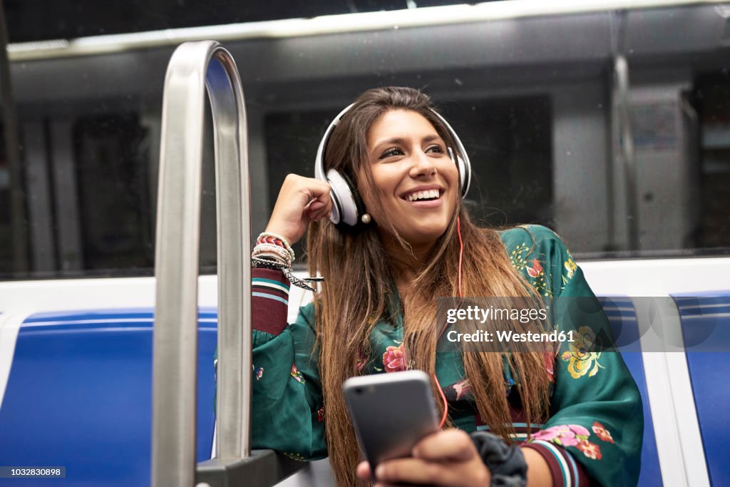 Portrait of happy woman listening music with headphones and smartphone in underground train