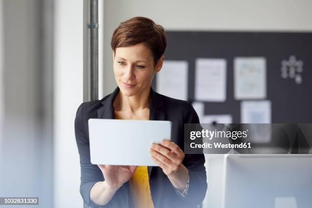 attractive businesswoman standing in office, using digital tablet - tablet pc stockfoto's en -beelden