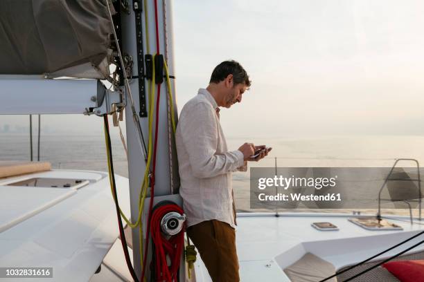 marure man on catamaran, using smartphone - mast sailing stock-fotos und bilder