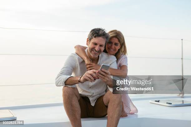 mature couple looking at smartphone, sitting on a sailing boat - premium with mobile stock pictures, royalty-free photos & images