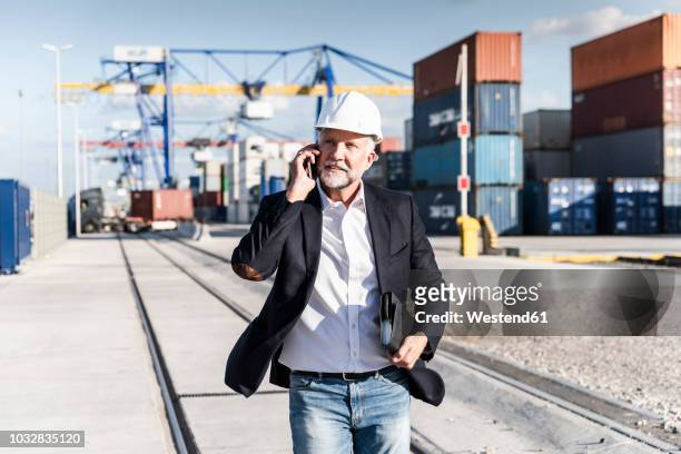 businessman at cargo harbour, wearing safety helmet, using smartphone - work accountability stock-fotos und bilder