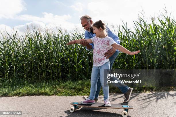 mature man helping little girl to learn skateboarding - skaten familie stock-fotos und bilder