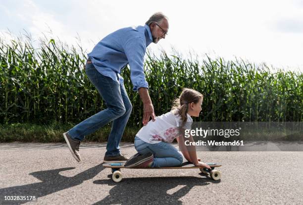 mature man helping little girl to learn skateboarding - granddaughter foto e immagini stock