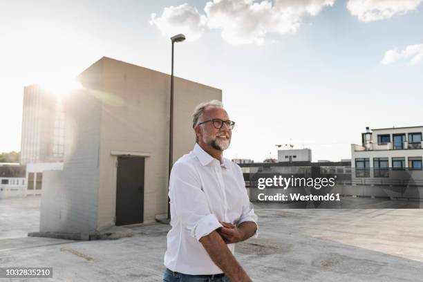 mature man standing on roof of a high-rise building, rolling up sleeves - business change stock-fotos und bilder