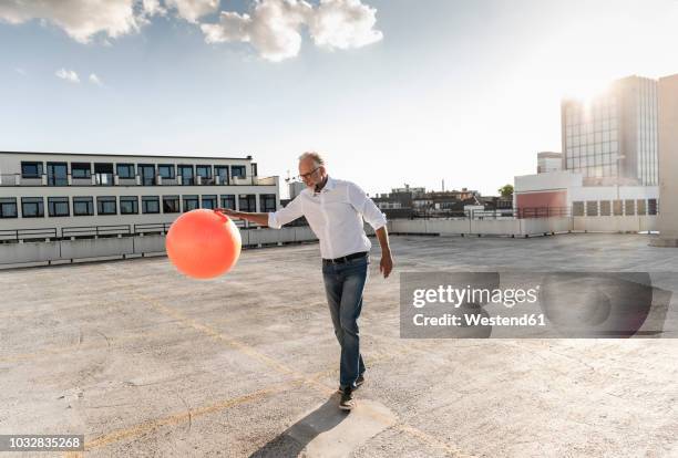 mature man playing with orange fitness ball on rooftop of a high-rise building - dribbling sport fotografías e imágenes de stock