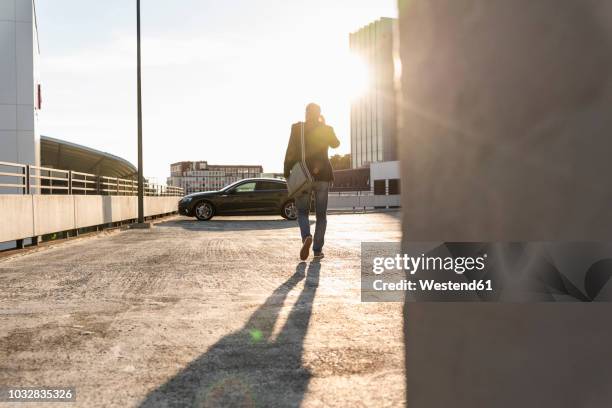 mature man walking on parking level to his car, talking at the phone - on the move rear view stockfoto's en -beelden