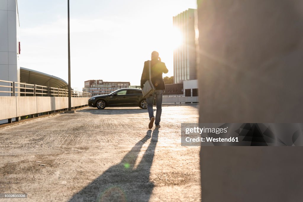 Mature man walking on parking level to his car, talking at the phone