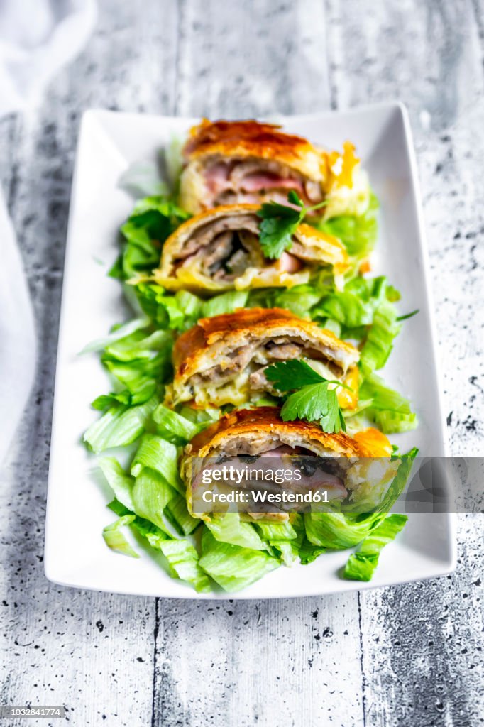 Swiss roll, puff pastry with sausage meat, cheese, onion, parsley and salad on plate