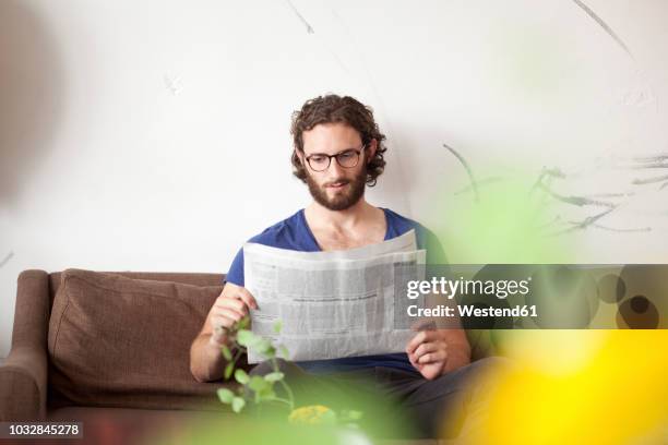 portrait of young man reading newspaper on couch in a coffee shop - junger mann liest zeitung stock-fotos und bilder