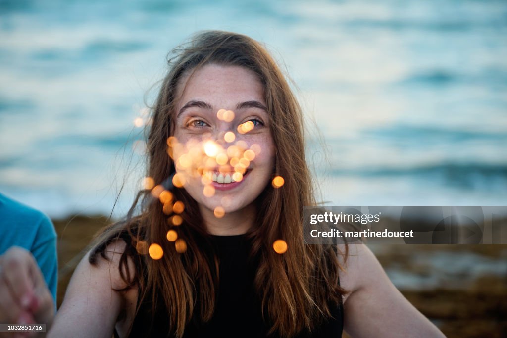 Young woman playing with sparklers on the beach at dusk