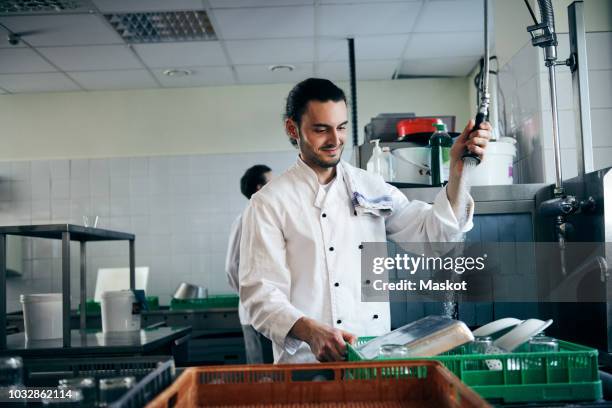 young chef spraying water on plates in commercial kitchen - restaurant cleaning stock pictures, royalty-free photos & images