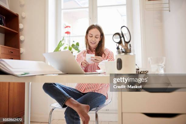 full length of young woman examining financial bill while working from home - house budget stock-fotos und bilder