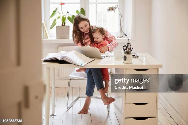 female accountant sitting with daughter while working on laptop at home - family budget stock-fotos und bilder