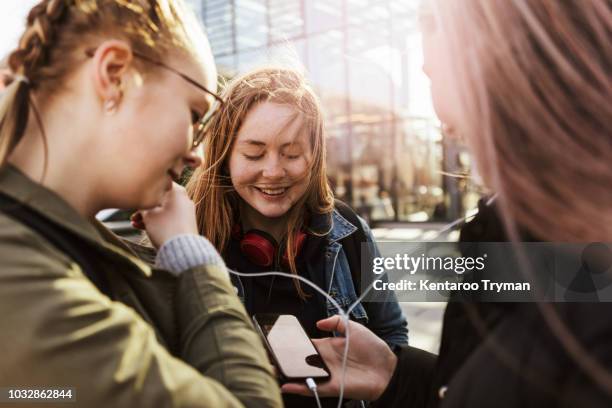 teenage girl looking at friends listening music through mobile phone in city - 3 teenagers mobile outdoors stock-fotos und bilder