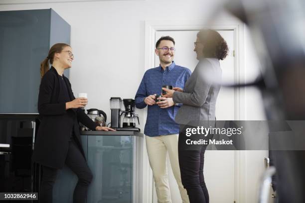 smiling business colleagues having coffee while talking at office - coffee break fotografías e imágenes de stock