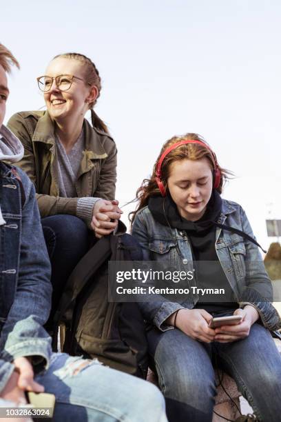 teenage girl using mobile phone while sitting with friends against clear sky - 3 teenagers mobile outdoors stockfoto's en -beelden