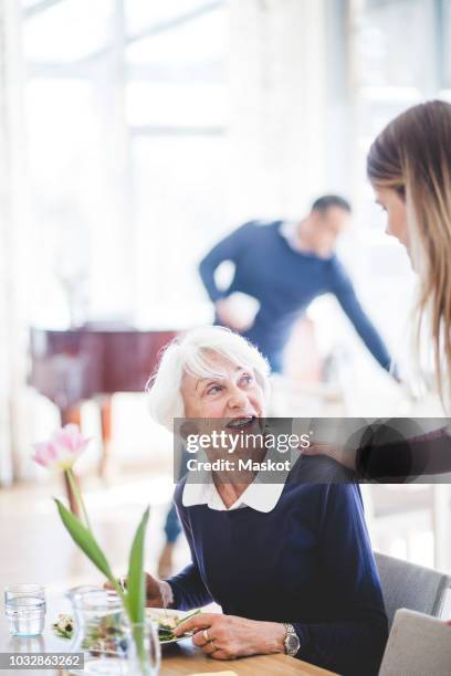 senior woman talking with granddaughter while having meal at table in nursing home - rentnersiedlung stock-fotos und bilder