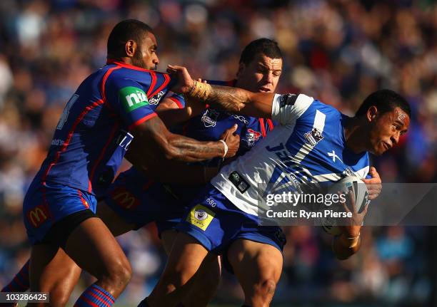 Ben Roberts of the Bulldogs is tackled by Wes Naiqama and Jarrod Mullen of the Knights during the round 22 NRL match between the Newcastle Knights...