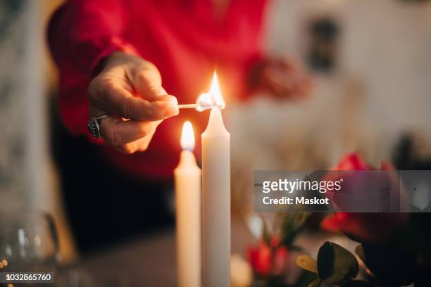 midsection of mature woman igniting candle on dining table in party at home - candela attrezzatura per illuminazione foto e immagini stock