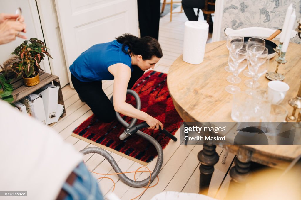 High angle view of mature woman cleaning hardwood floor with vacuum cleaner after party at home