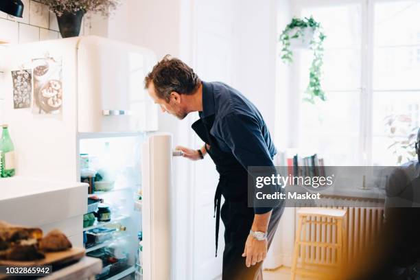mature man looking into refrigerator while standing at kitchen - abierto fotografías e imágenes de stock