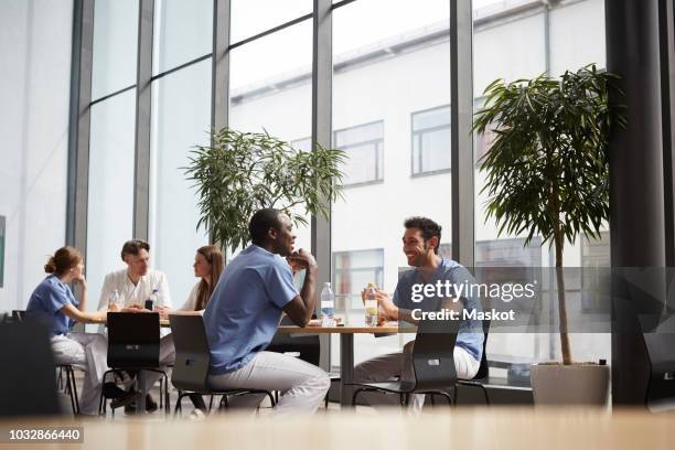 smiling multi-ethnic medical team sitting at cafeteria in hospital - cafeteria stock pictures, royalty-free photos & images