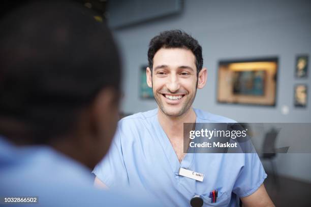 smiling male nurse talking with coworker at cafeteria in hospital - nametag stockfoto's en -beelden