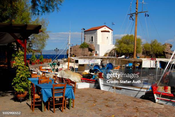 restaurant tavern, chairs and tables outside, small fishing boats in the harbor of skala sikaminea, greek orthodox chapel, lesbos island, aegean sea, greece - lesbos stock pictures, royalty-free photos & images