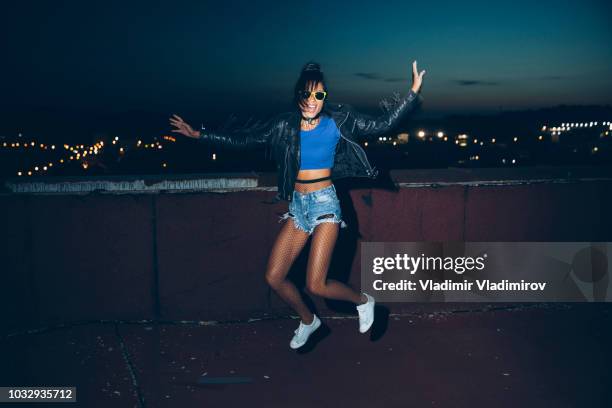 beautiful woman with leather jacket jumping on rooftop - spring city break stock pictures, royalty-free photos & images